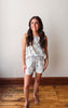 Woman wearing a floral outfit standing on a wooden floor against a plain wall.
