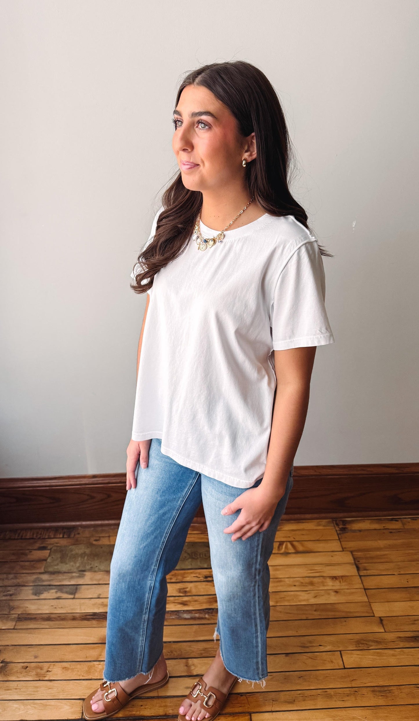 Woman wearing a white blouse and blue jeans standing on a wooden floor.
