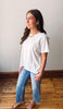Woman wearing a white blouse and blue jeans standing on a wooden floor.