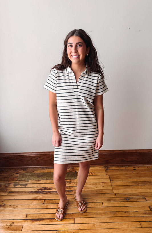 Woman wearing a striped dress standing on a wooden floor with a white wall background