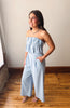 Woman wearing a light blue strapless jumpsuit standing on a wooden floor.