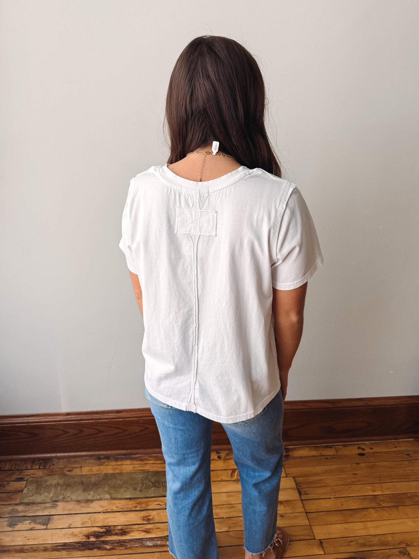 Person wearing a white blouse and blue jeans standing against a plain wall.