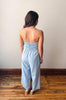Woman wearing a light blue strapless jumpsuit standing on a wooden floor against a plain wall.