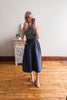Woman taking a mirror selfie wearing a striped top and navy skirt in a room with wooden flooring and a decorative cabinet.