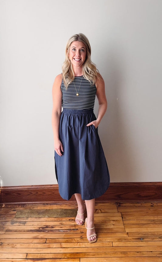 Woman wearing a navy dress standing on a wooden floor against a white wall