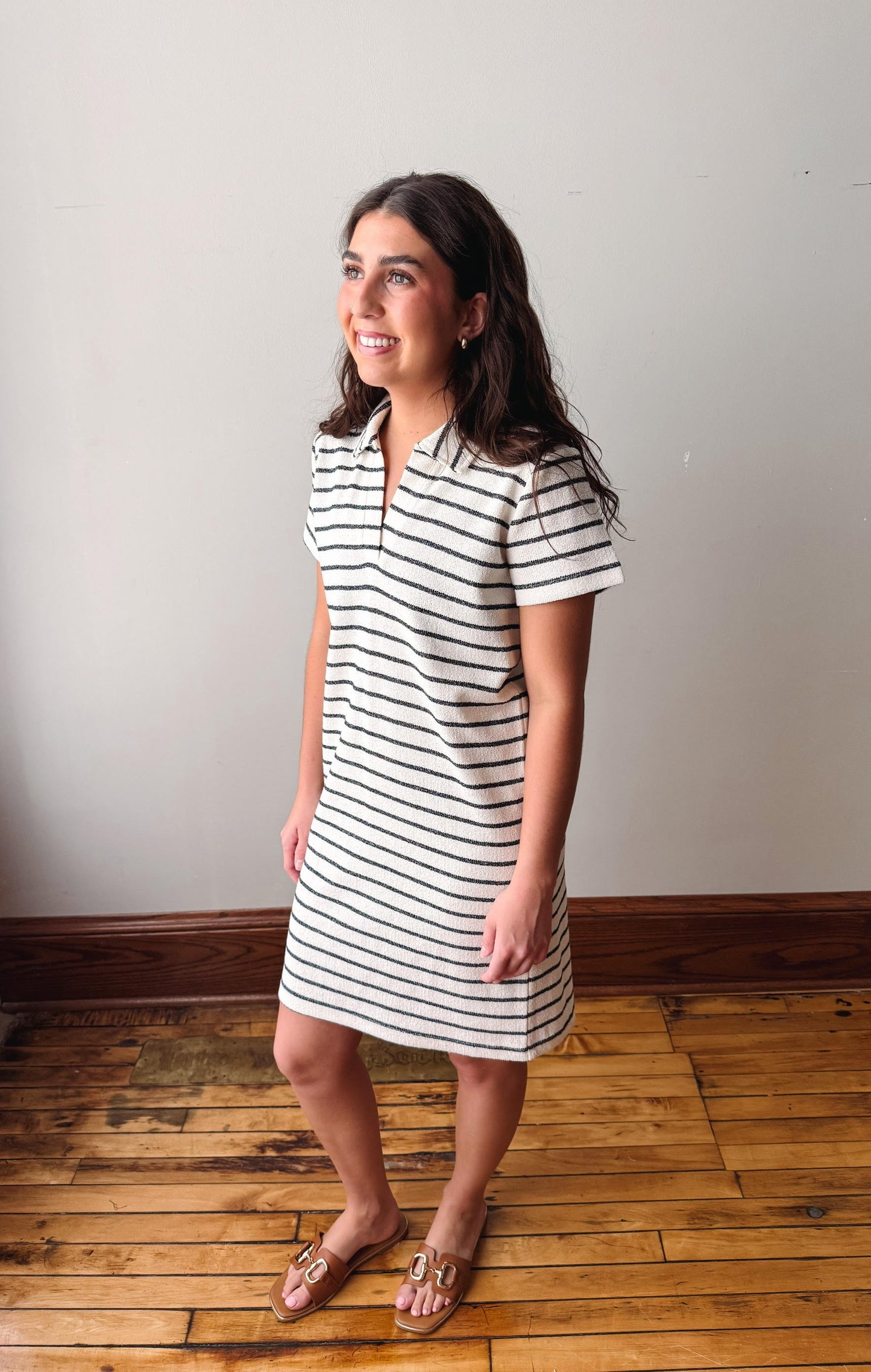 Woman wearing a black and white striped dress standing on a wooden floor with a plain wall background