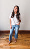 Woman wearing a white t-shirt and blue jeans standing on a wooden floor with a white wall background