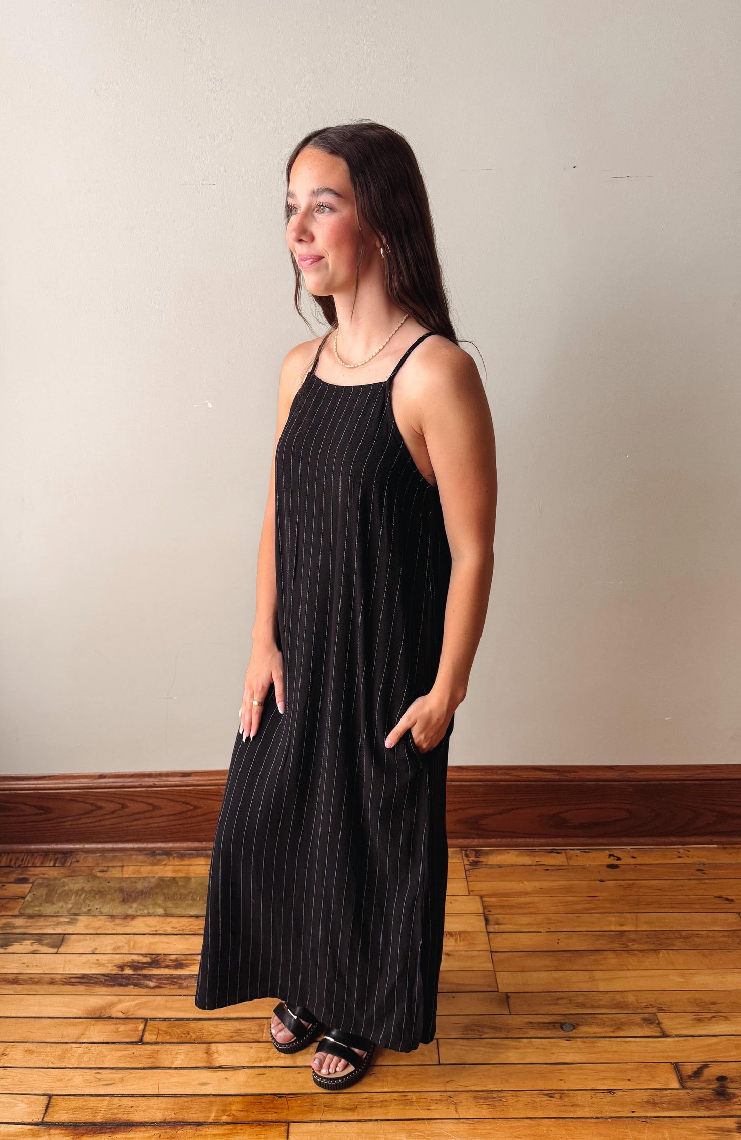 Woman wearing a black dress standing on a wooden floor with a plain wall background