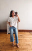 Woman taking a mirror selfie wearing a white blouse and blue jeans in a room with wooden flooring.