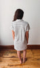 Person wearing a black and white striped dress standing on a wooden floor with a white wall background