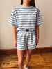 A person wearing a matching two-piece loungewear set with a light blue and navy blue horizontal stripe pattern, standing in an indoor room with a wood floor and beige wall.