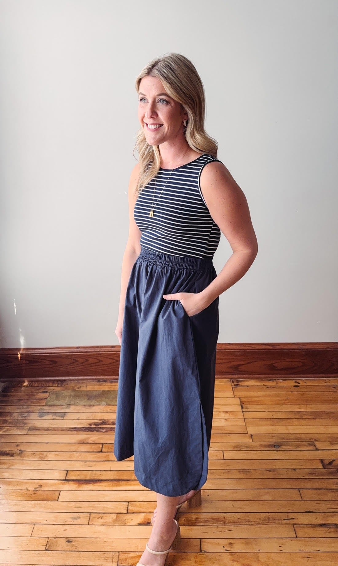 Woman wearing a striped top and blue skirt standing on a wooden floor.