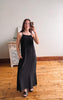 Woman taking a mirror selfie wearing a black sleeveless dress in a room with wooden flooring.