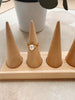 A gold ring with a large white pearl center stone displayed on a light wood cone ring holder, with a white ceramic pot in the background.