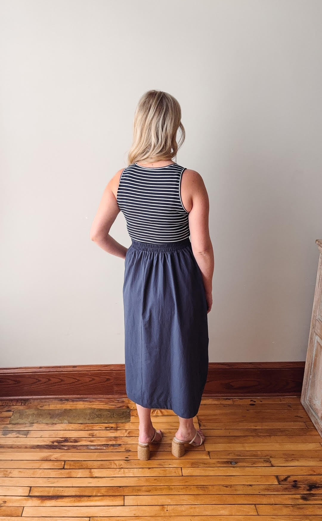 Woman wearing a striped top and denim skirt standing on a wooden floor with a white wall background