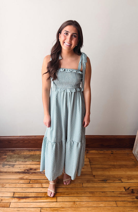 Woman wearing a green checkered dress standing on a wooden floor with a white wall background