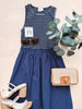 Navy blue dress with striped top, sunglasses, sandals, and a woven handbag on a light background.