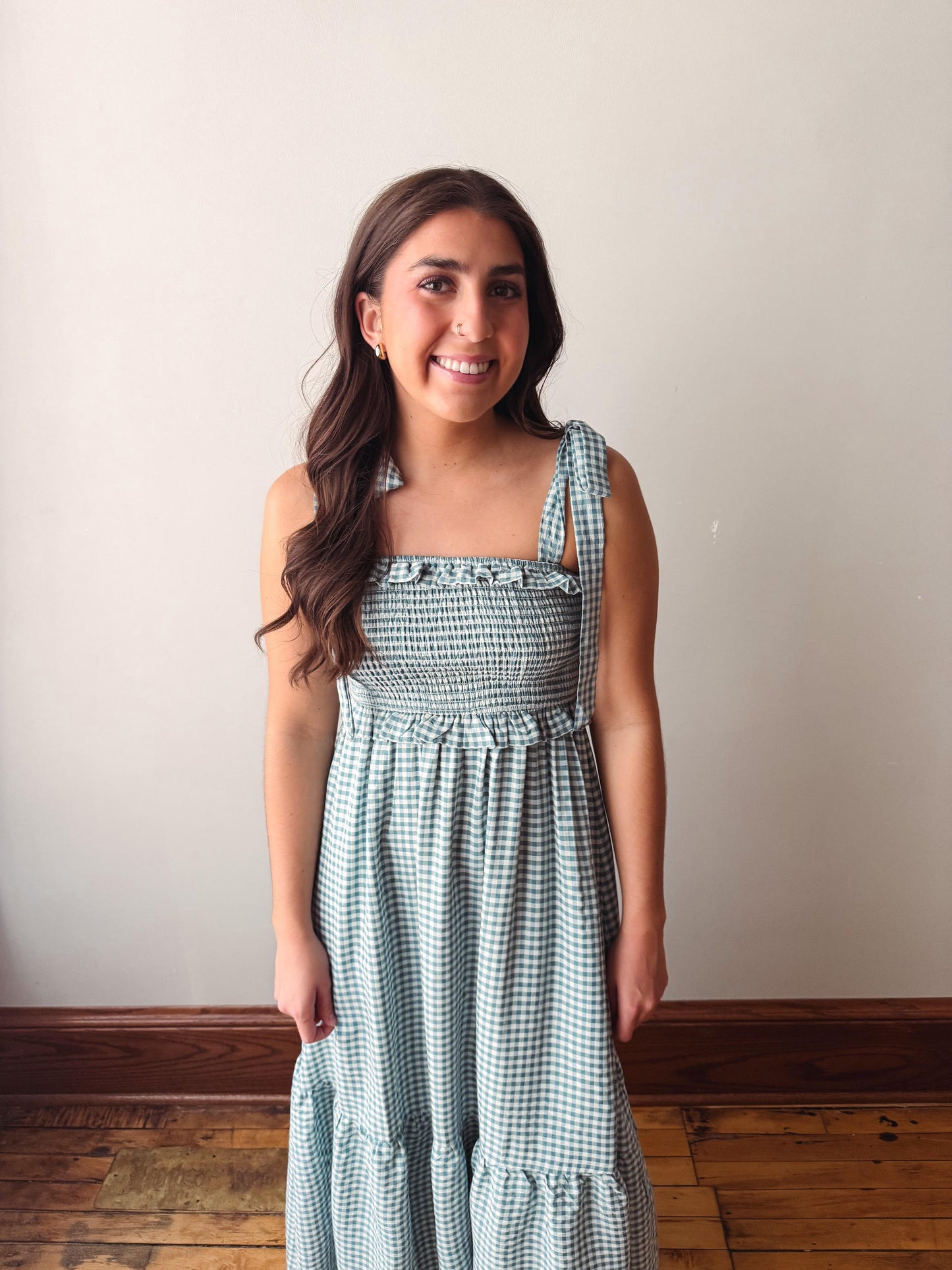 Woman wearing a green checkered dress standing against a plain wall.