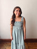 Woman wearing a green checkered dress standing against a plain wall.