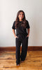 Woman wearing a black outfit standing on a wooden floor with a white wall background