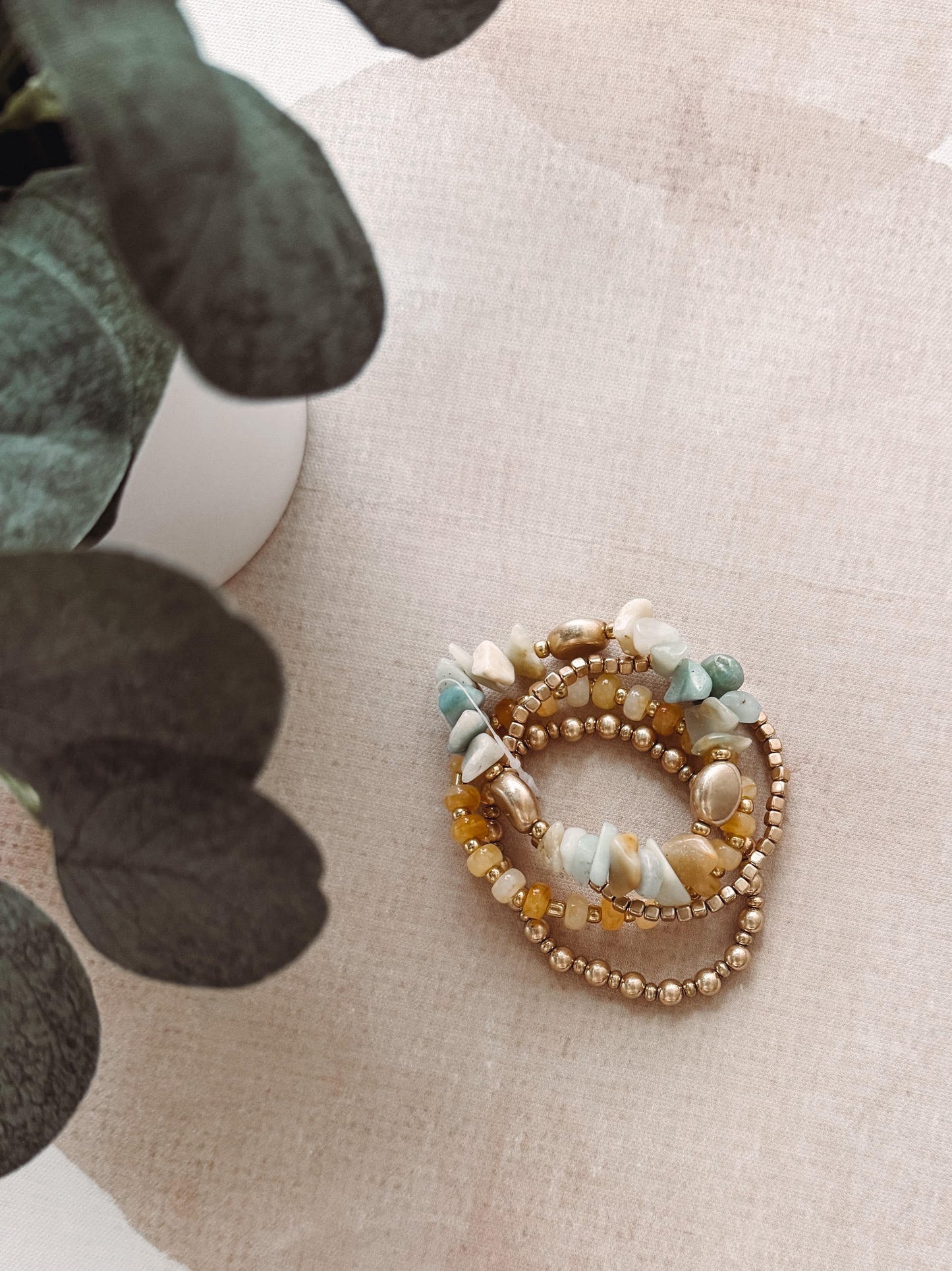 Set of beaded bracelets on a textured surface with a plant in the background
