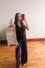 Person taking a mirror selfie wearing a black outfit in a room with wooden flooring and a decorative cabinet.