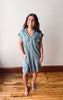 Woman wearing a light blue dress standing on a wooden floor with a white wall background