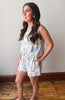 Woman wearing a floral romper standing against a plain wall.