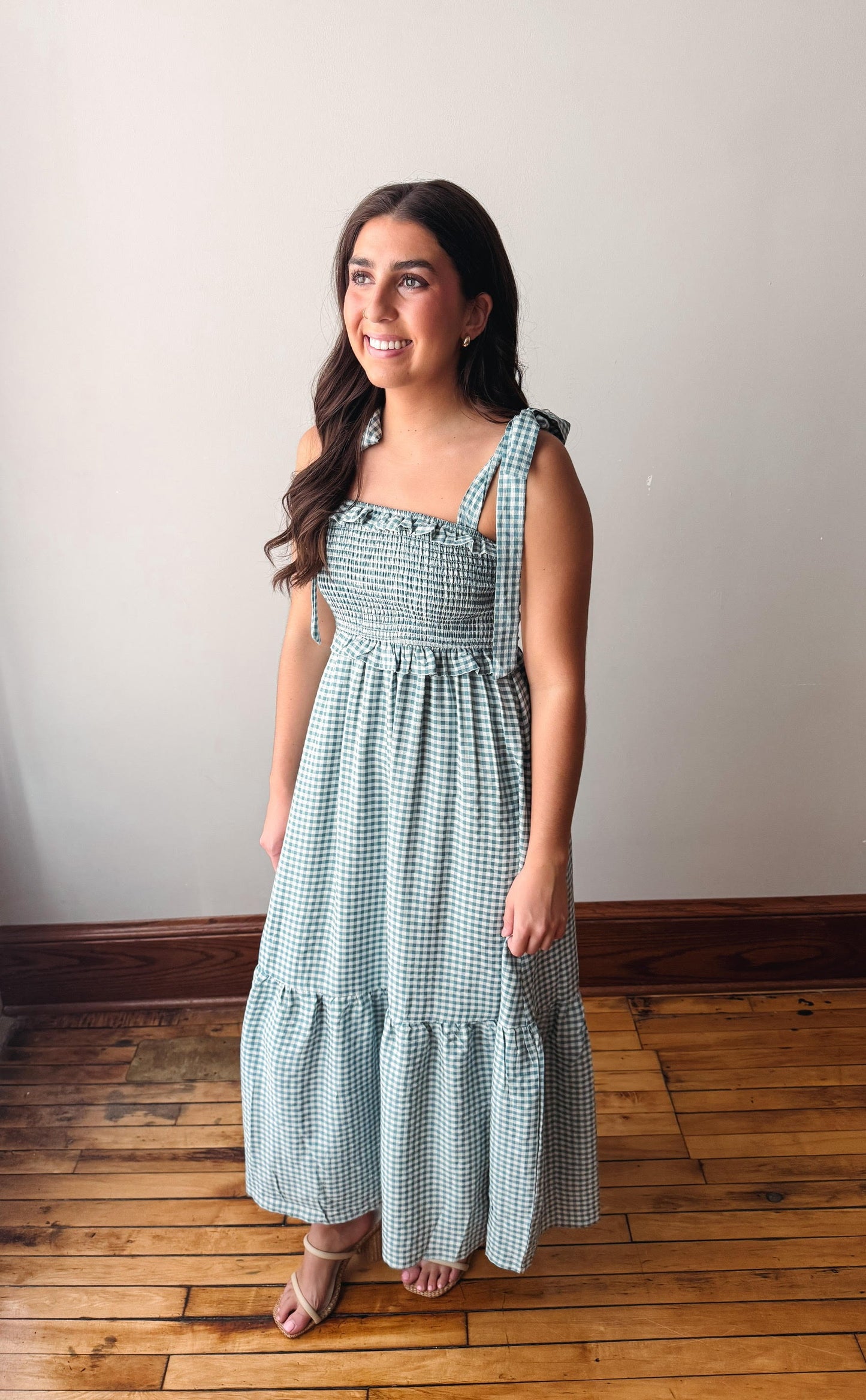 Woman wearing a light blue checkered dress standing on a wooden floor.