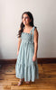 Woman wearing a light blue checkered dress standing on a wooden floor.