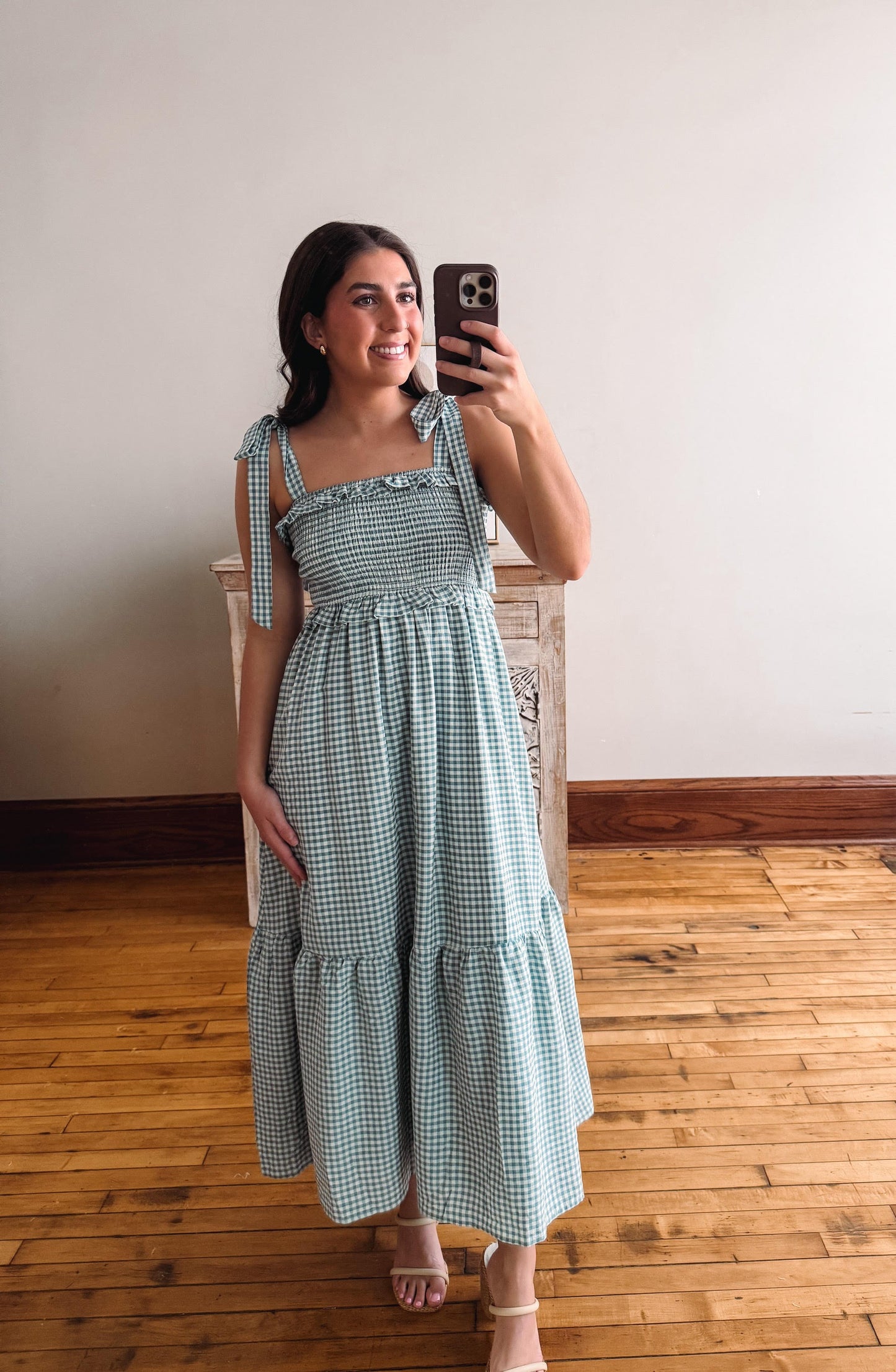 Woman taking a selfie in a green checkered dress on a wooden floor.