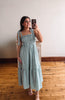 Woman taking a selfie in a green checkered dress on a wooden floor.