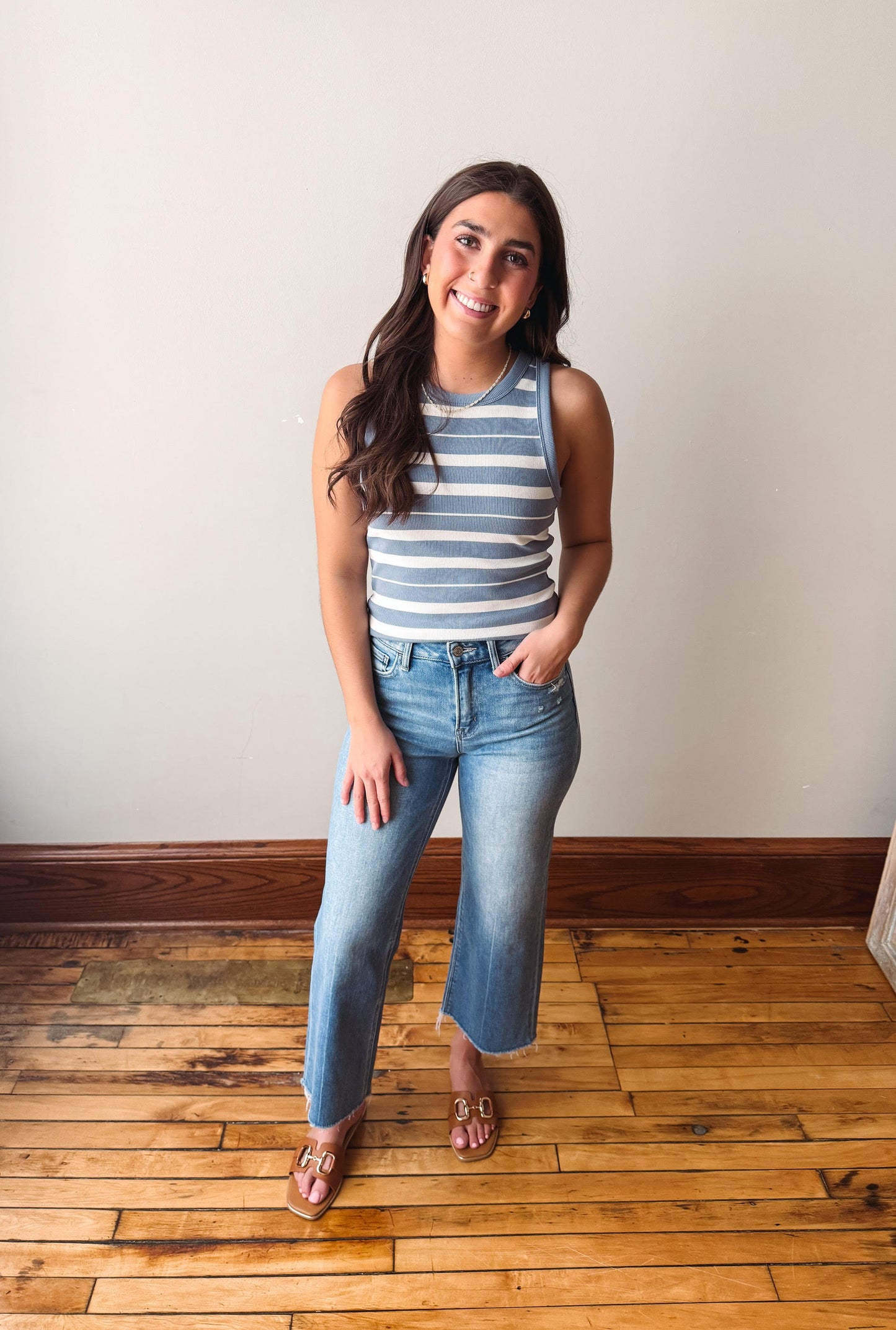 Woman wearing a striped tank top and jeans standing on a wooden floor.