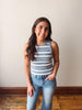 Woman wearing a striped tank top and jeans standing against a plain wall.