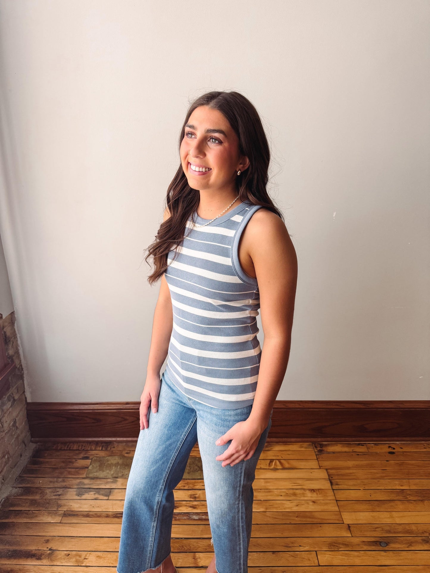 Woman wearing a striped tank top and jeans standing against a plain wall.