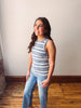 Woman wearing a striped tank top and jeans standing against a plain wall.