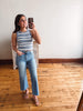 Woman taking a mirror selfie wearing a striped tank top and jeans in a room with wooden flooring.
