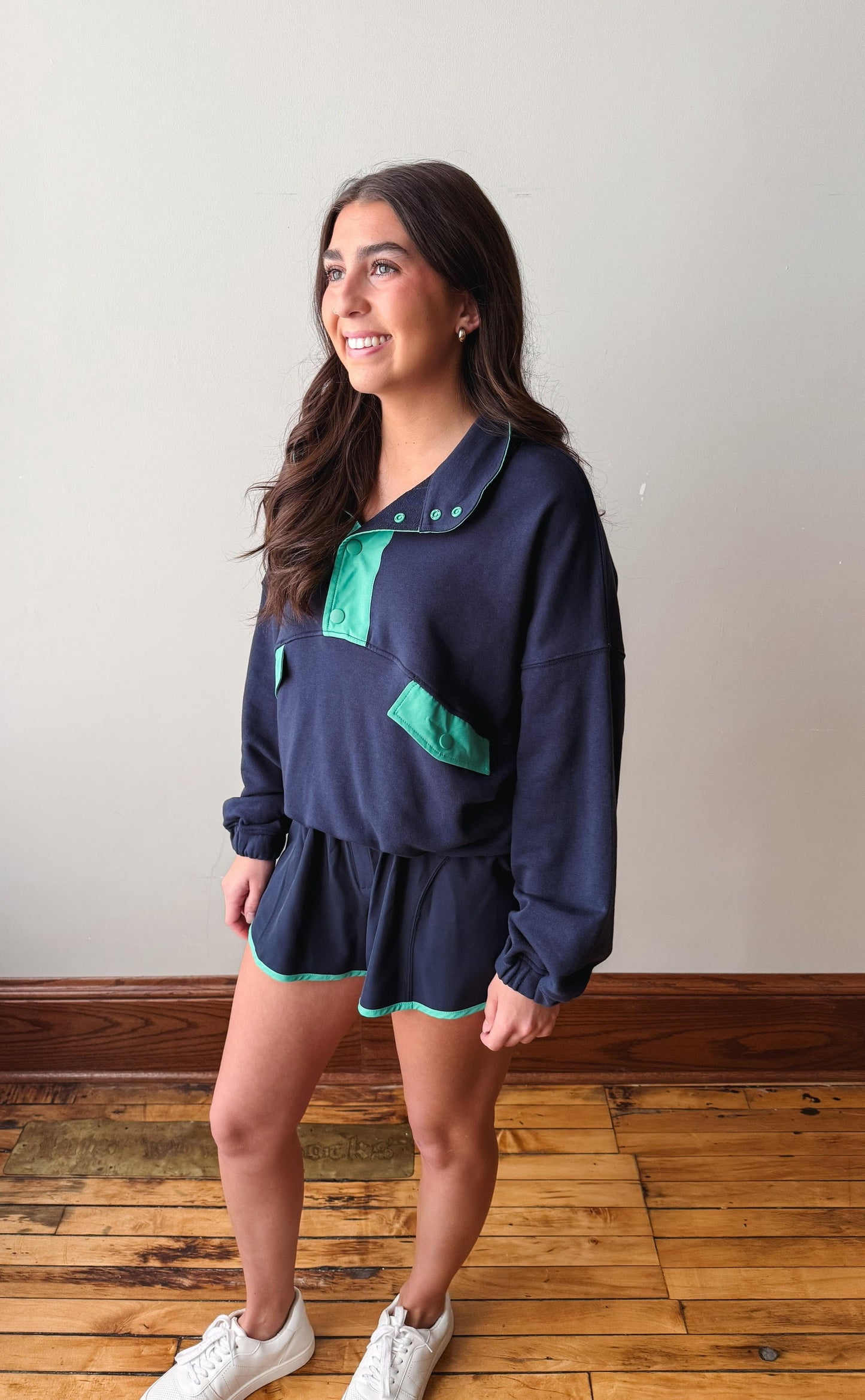 Woman wearing a navy blue outfit with green accents standing on a wooden floor.