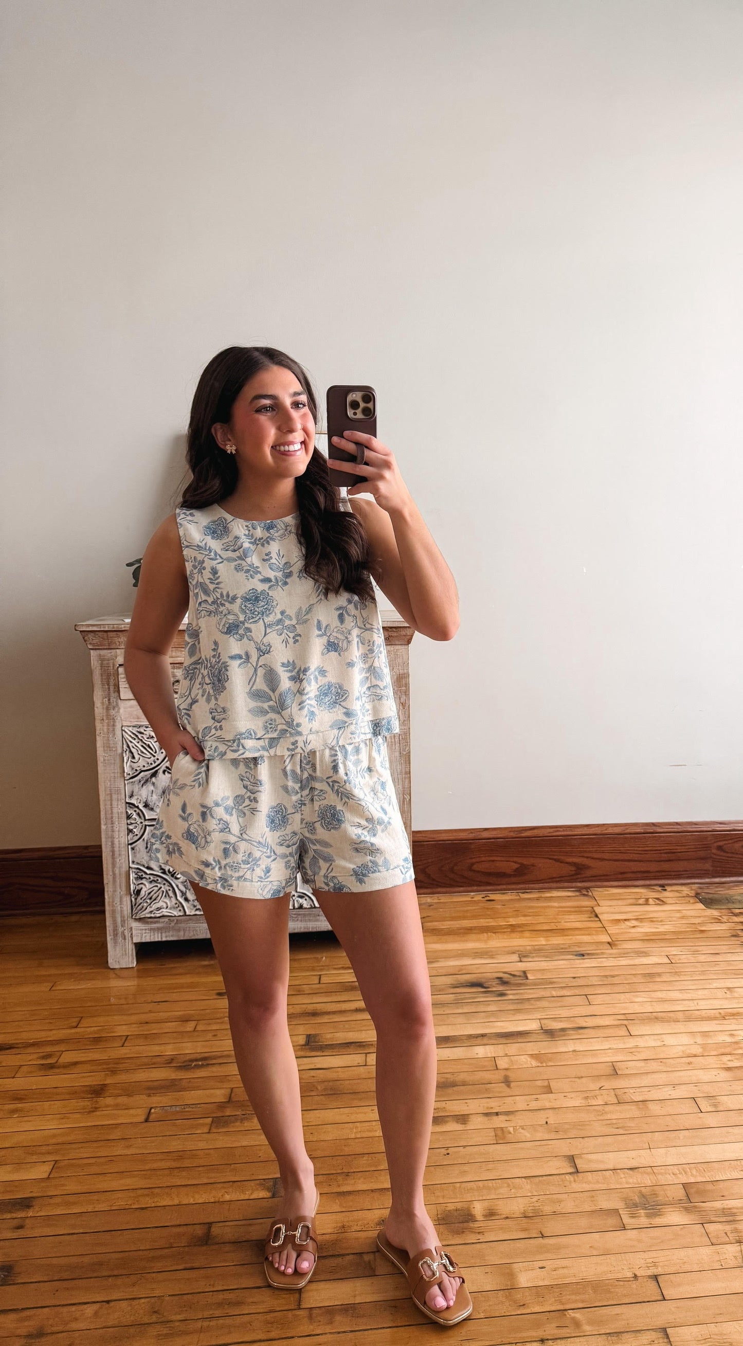 Woman taking a mirror selfie wearing a floral dress on a wooden floor.