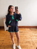 Person taking a mirror selfie wearing a navy outfit with green accents in a room with wooden flooring.