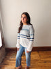 Woman wearing a striped sweater and jeans standing in a room with wooden flooring and white walls.