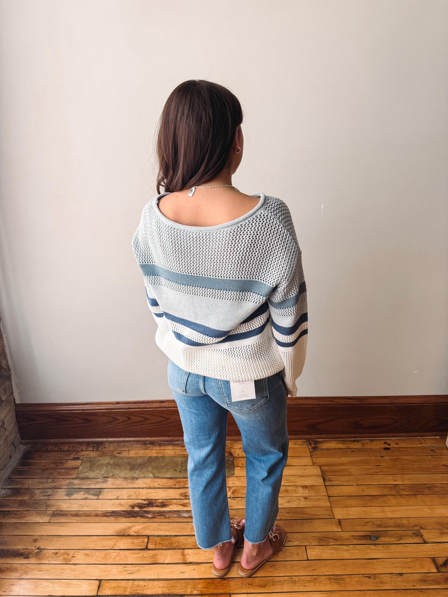 Person wearing a striped sweater and jeans standing against a plain wall.