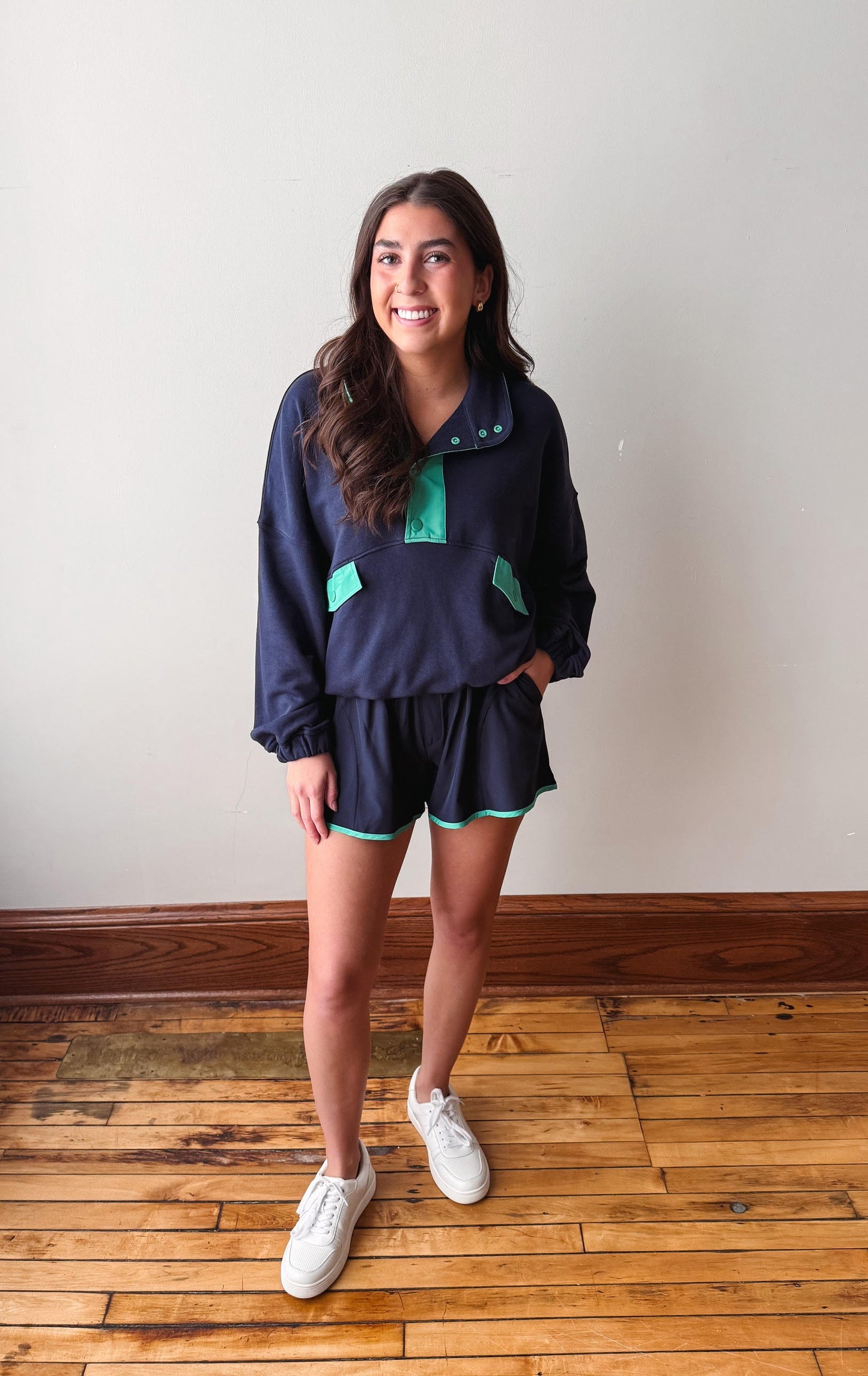 Woman wearing a navy blue outfit with green accents on a wooden floor.