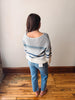 Person wearing a striped sweater and jeans standing against a plain wall.