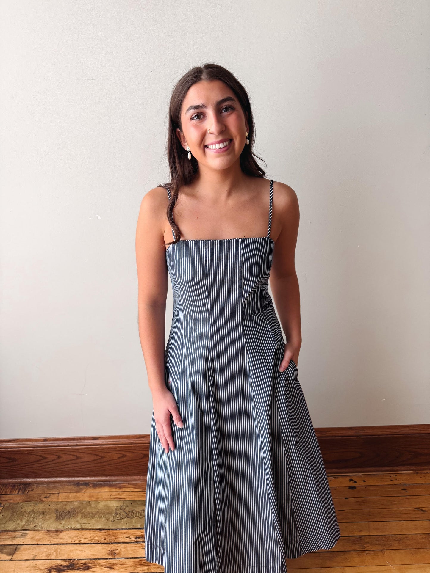 Woman wearing a blue striped dress standing against a plain wall.