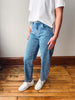 A person wearing light blue denim jeans with small white embroidered dots, styled with a white t-shirt and white sneakers, standing on a wooden floor against a plain wall.