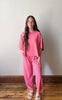 Woman wearing a pink outfit standing against a white wall.