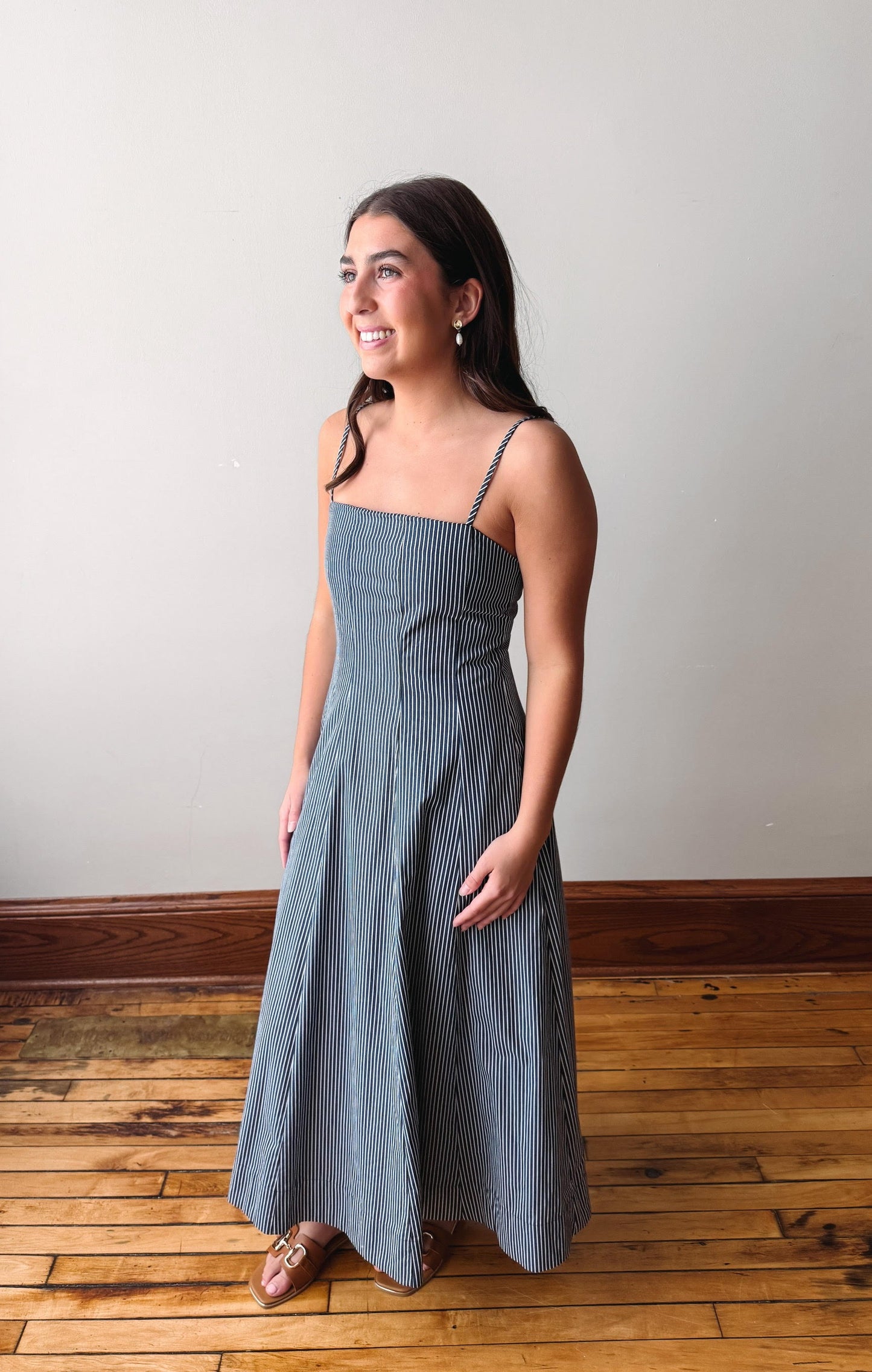 Woman wearing a blue striped dress standing on a wooden floor with a white wall background
