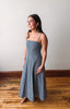 Woman wearing a blue striped dress standing on a wooden floor with a white wall background