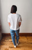 A person viewed from behind wearing a white short-sleeve t-shirt and blue jeans with small white star patterns, standing on a wooden floor against a plain wall.